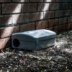 Grey Metal external rodent rat bait station outside against a brick wall close up.