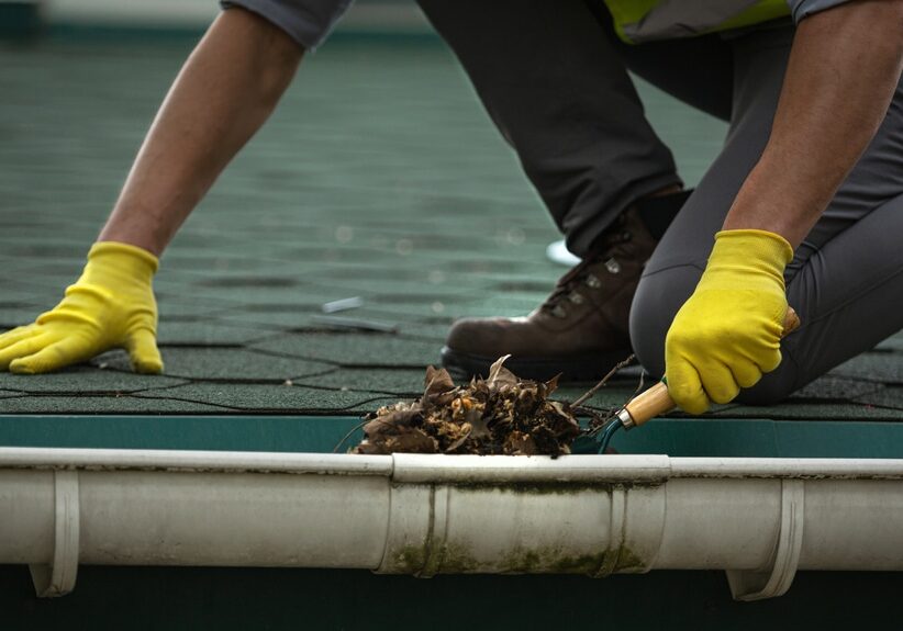 A man worker is cleaning a clogged roof gutter from dirt