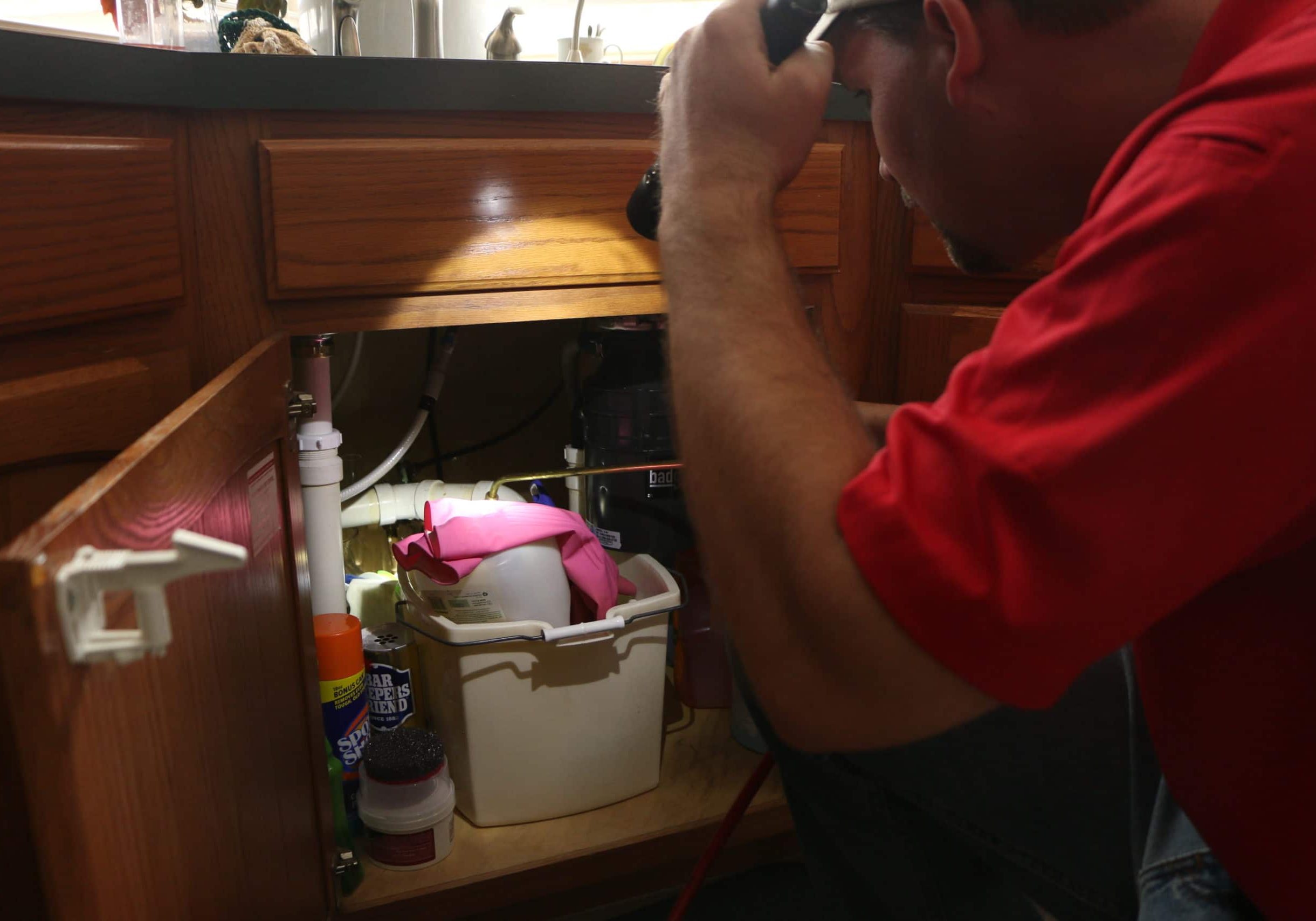 Pest control technician shining flashlight under kitchen sink