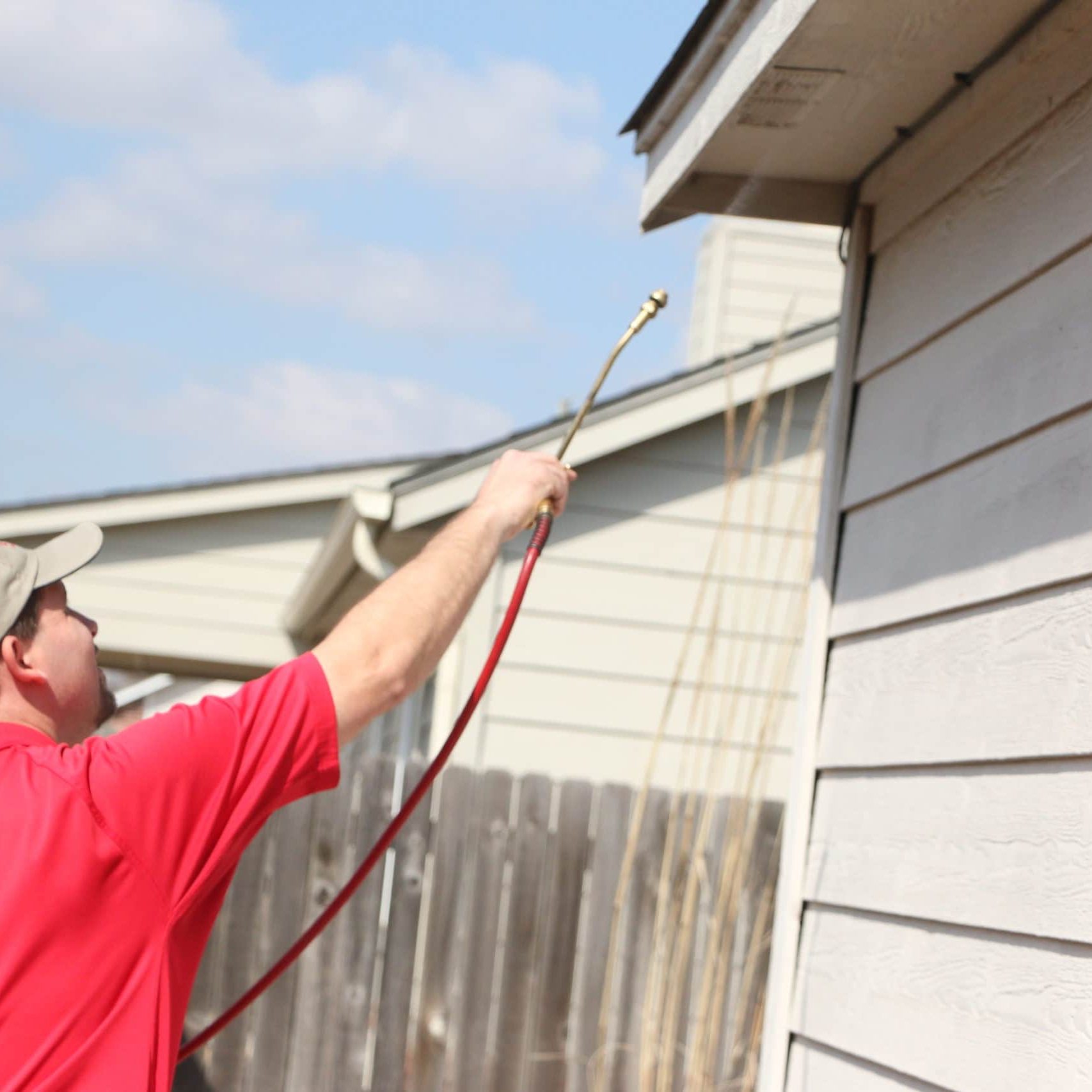 Pest control technician treating home outside under eves