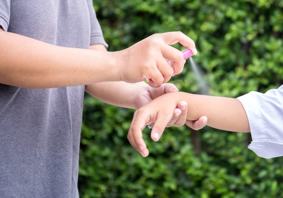 Spraying insect repellents on her kid's arm in the garden