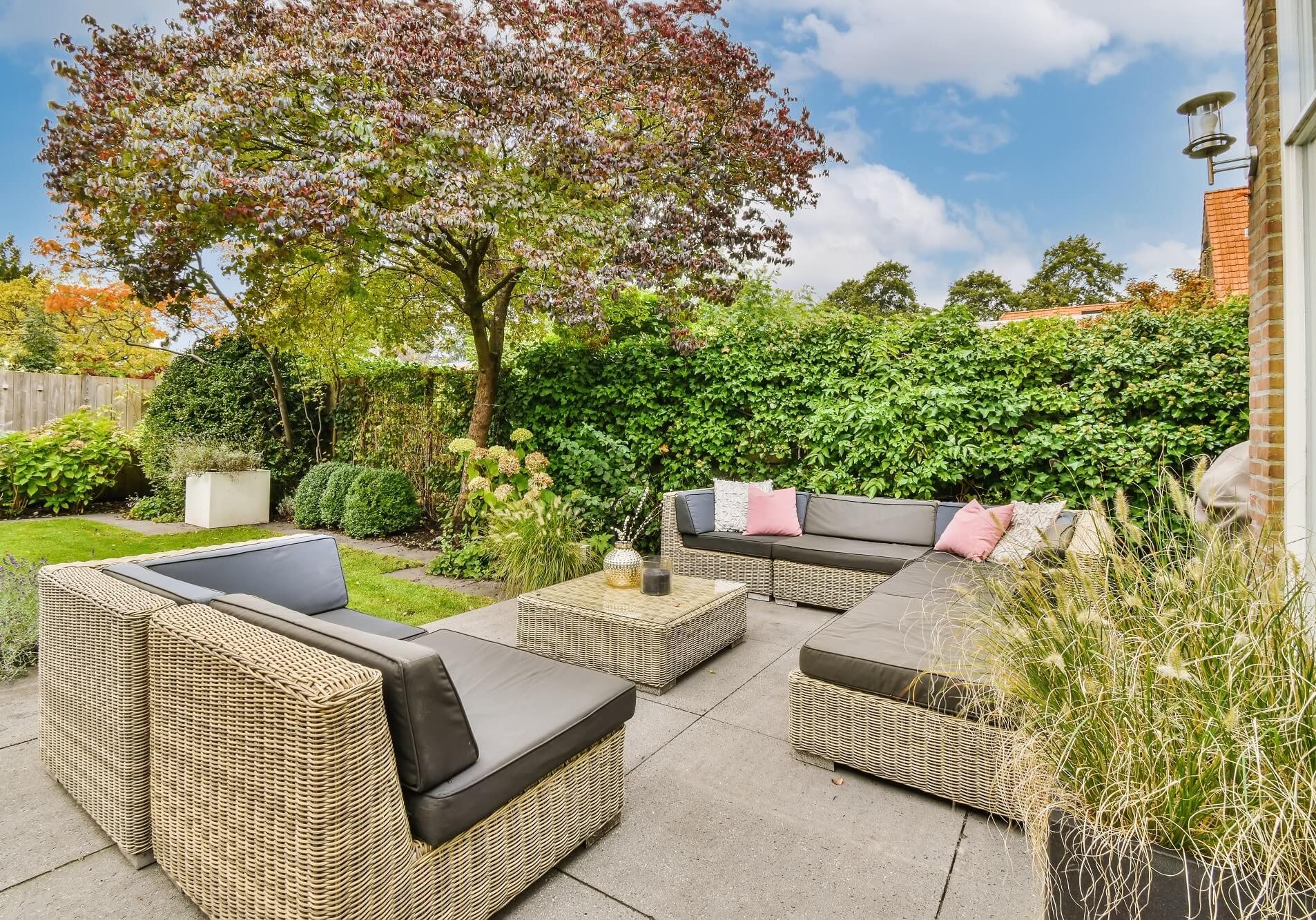 an outdoor living area with wickers and plants on the ground, surrounded by shrubs and trees in springtime