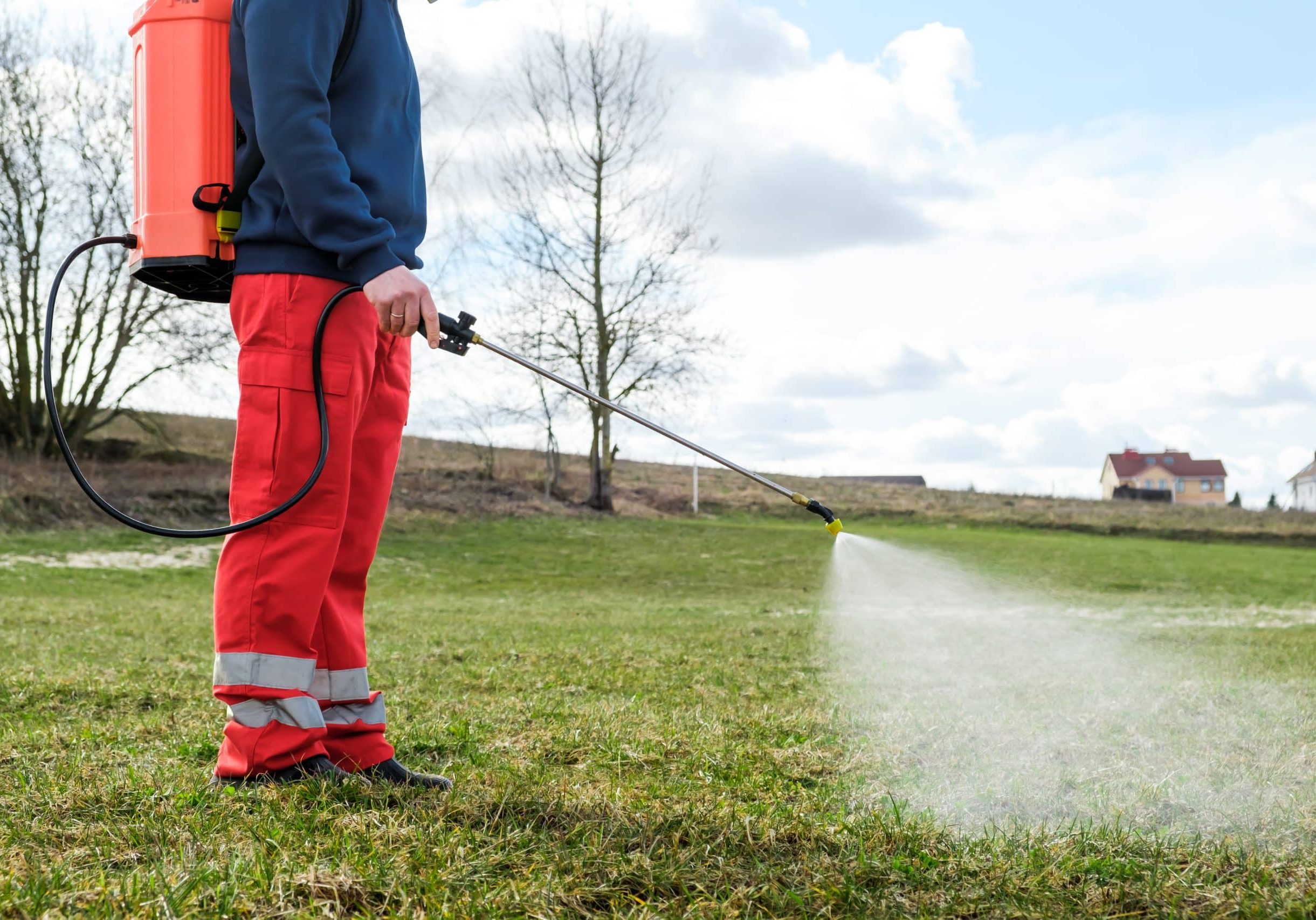 Farmer spraying pesticide on lawn field wearing protective clothing