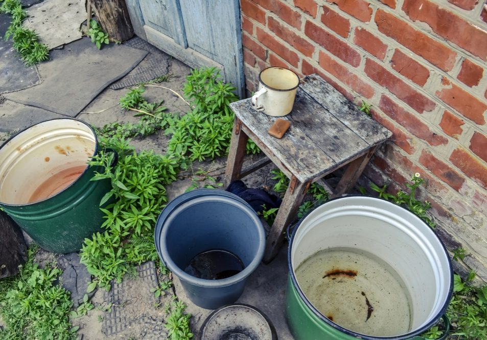 Buckets,And,Large,Pans,Of,Water,Stand,Outside,Near,A Buckets and large pans of water stand outside near a red brick wall - top view.